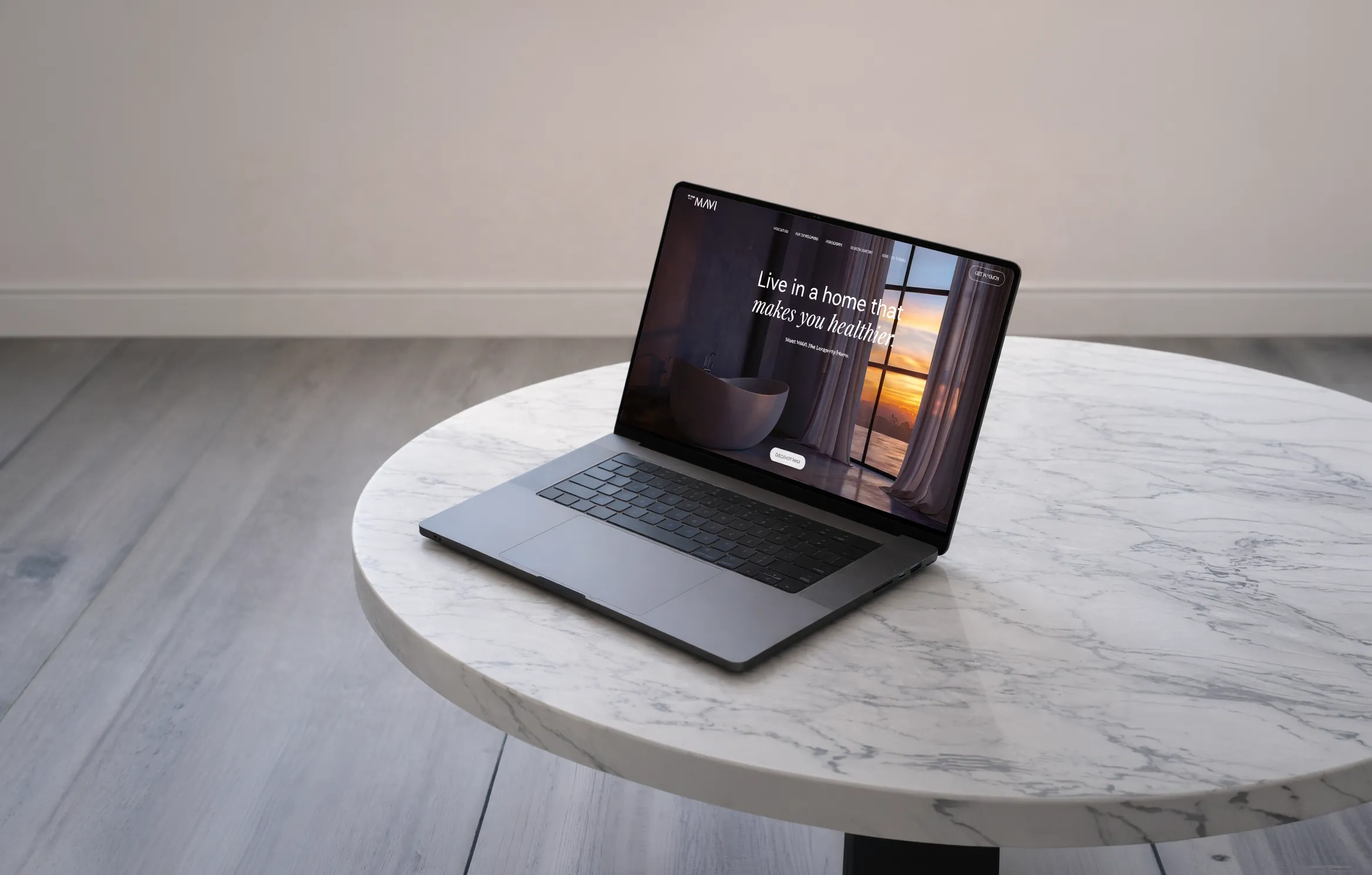 Open laptop on a round white marble table displaying a website homepage with the text Live in a home that makes you healthier.